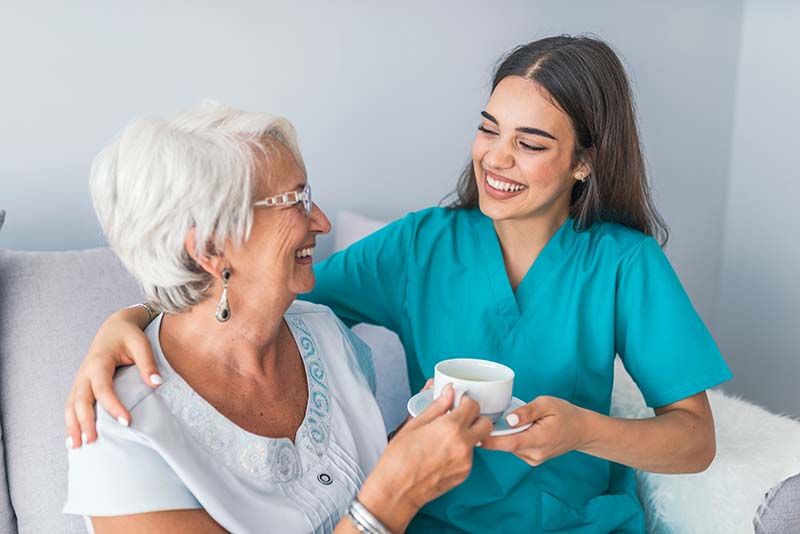 Home care nurse serving tea to elderly woman